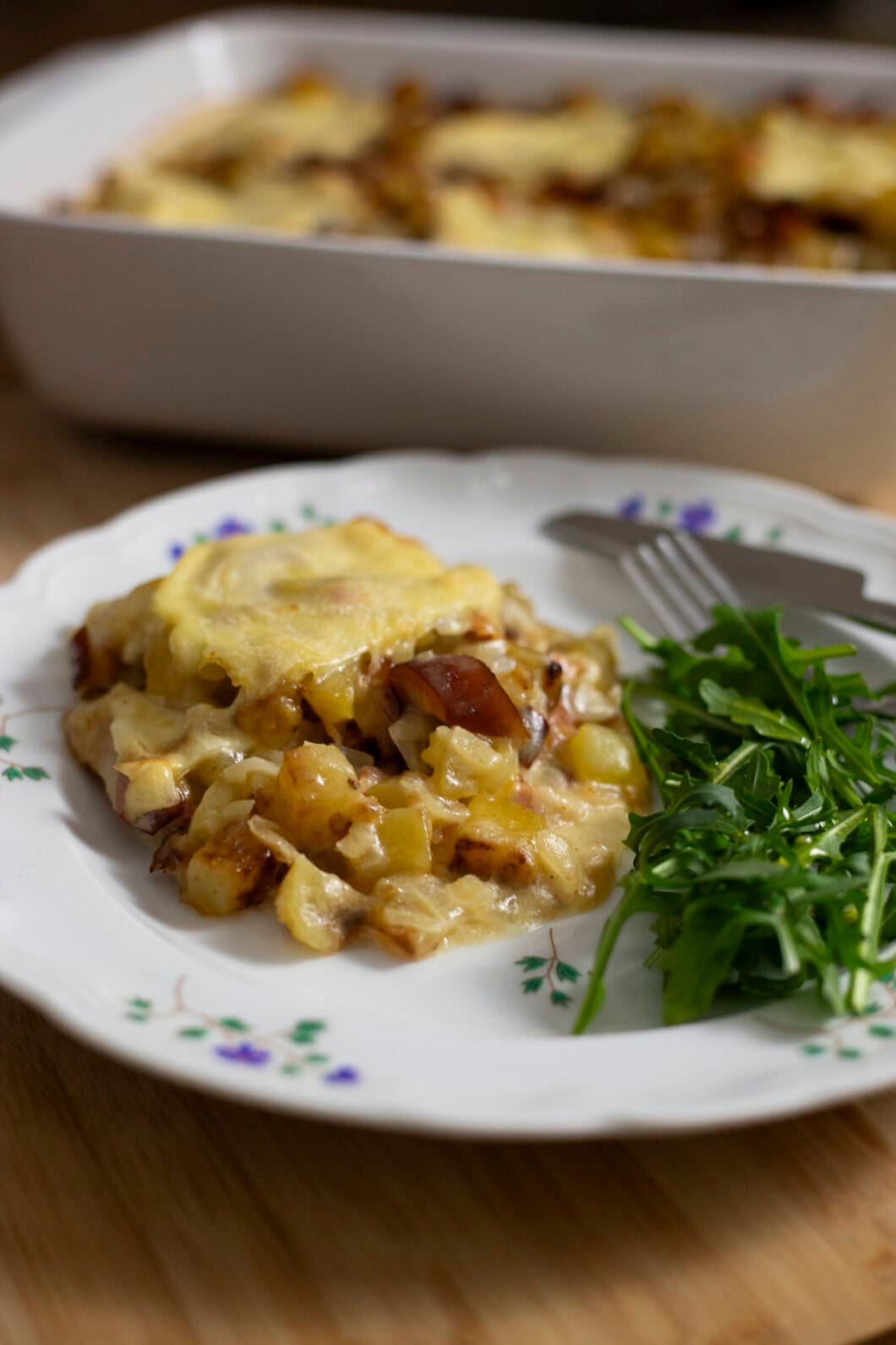 Zoomed image of a serving of Tartiflette, a French potato gratin with Reblochon cheese, with a side of salad