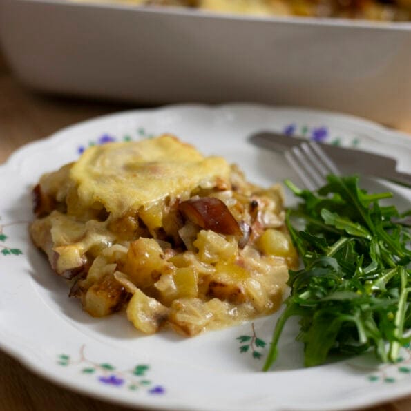 Zoomed image of a serving of Tartiflette, a French potato gratin with Reblochon cheese, with a side of salad