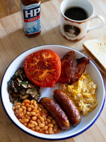 English breakfast with sausage, bacon, egg, beans, mushrooms and grilled tomato