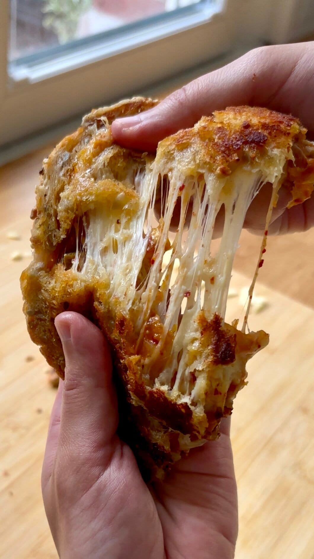 Kimchi grilled cheese sandwich being pulled apart, showing long, stretchy melted cheese strands with bits of red kimchi inside and a golden, crispy bread crust.