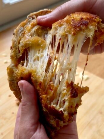Kimchi grilled cheese sandwich being pulled apart, showing long, stretchy melted cheese strands with bits of red kimchi inside and a golden, crispy bread crust.