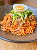 Bibim guksu — Korean spicy cold noodles with gochujang sauce, topped with cucumber matchsticks, sesame seeds and a halved boiled egg, served in a stone bowl