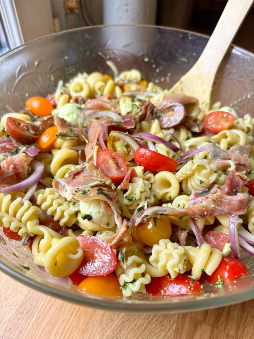 Pesto pasta salad with tomatoes, cured ham, red onions and mini mozzarella balls
