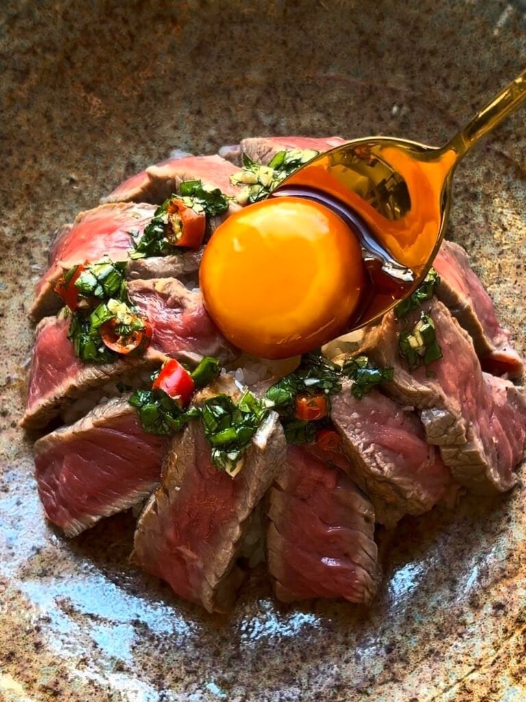 rice bowl covered with beef slices and a marinated egg yolk + Thai chimichurri sauce