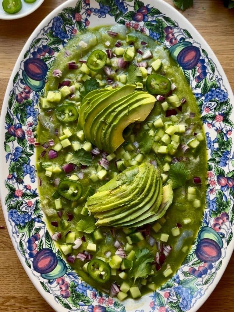 large oval dish filled with aguachile -raw shrimps, a green marinade with cucumber and fresh green chilies plus cubed cucumber onion cilantro and sliced green chilies and avocado slices
