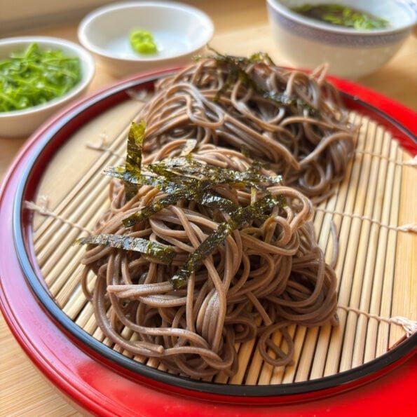 Japanese bamboo plate with two soba noodles nest, a dipping sauce bowl with mentsuyu and water, scallions and wasabi on the side