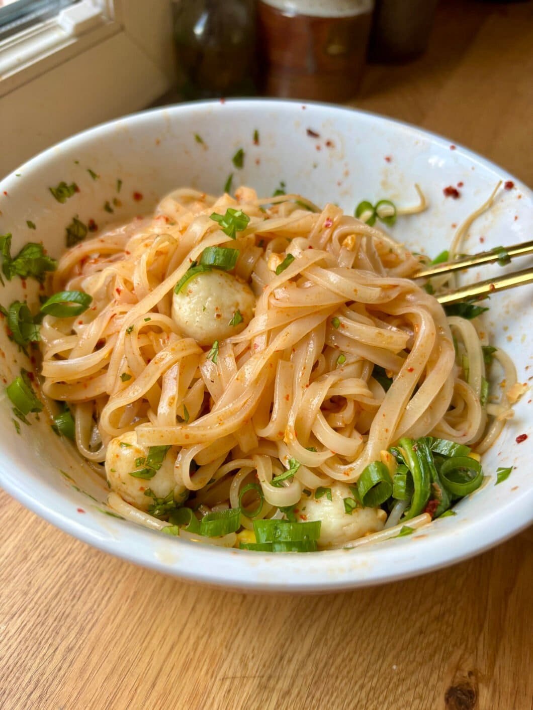 Shiny rice noodles with fishballs and green onion, coated in a luscious reddish sauce