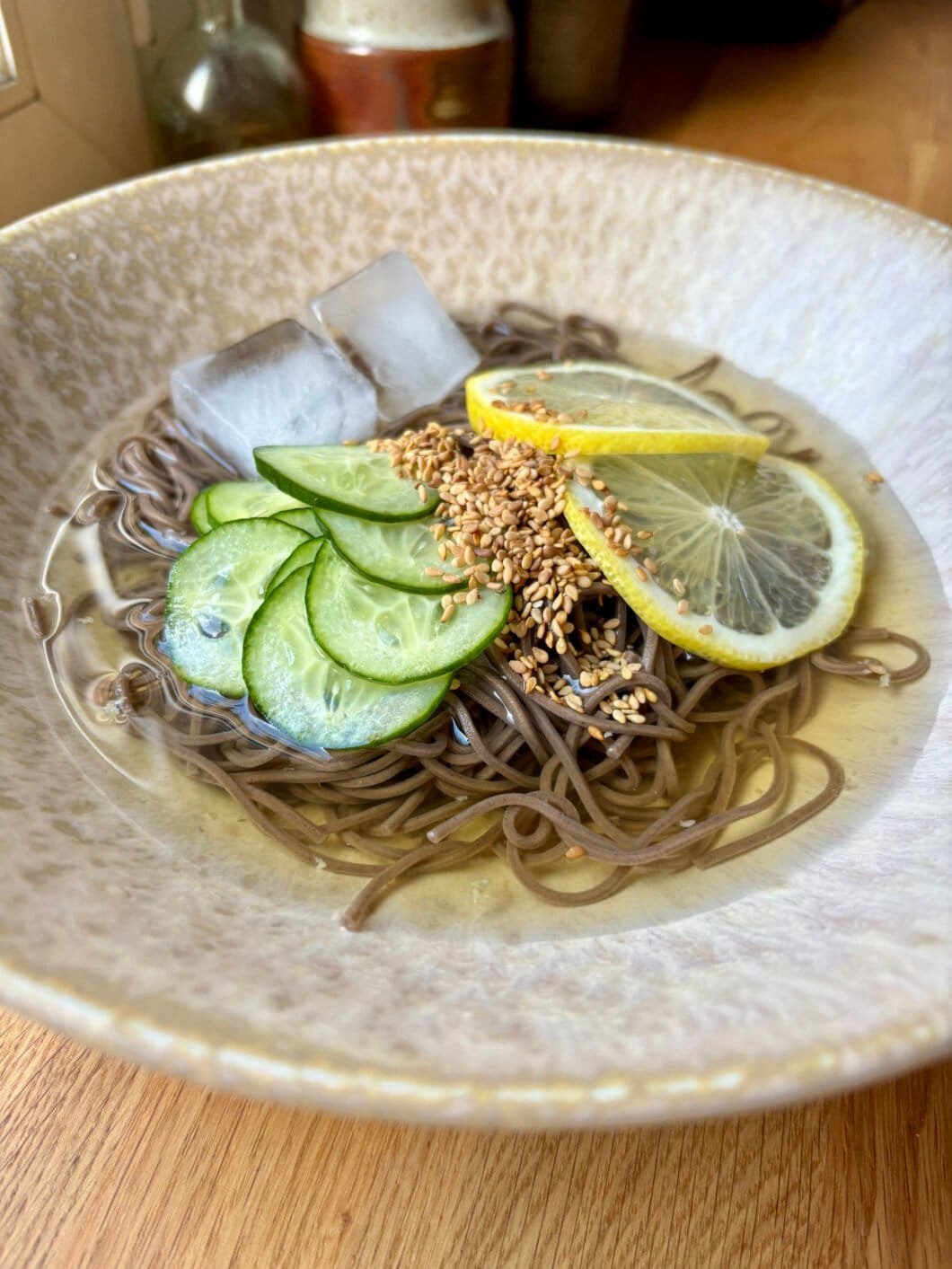 Soba noodles in a very clear broth, topped with extra thin cucumber slices and lemon slices, sesame seeds and two ice cubes