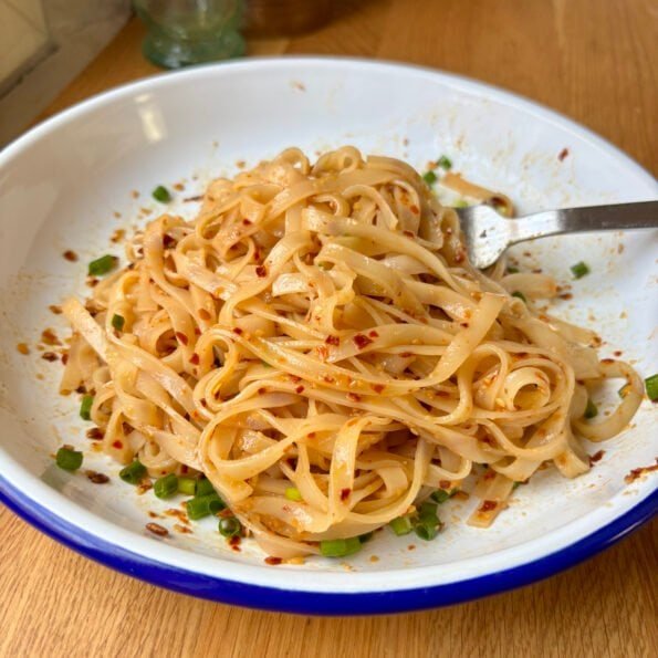 Rice noodles coated in a shiny, garlicky and spicy semi-transparent sauce, topped with scallions