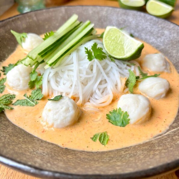 thin noodles in a orangey cold red curry broth topped with fishballs, cilantro, cucumber and lime