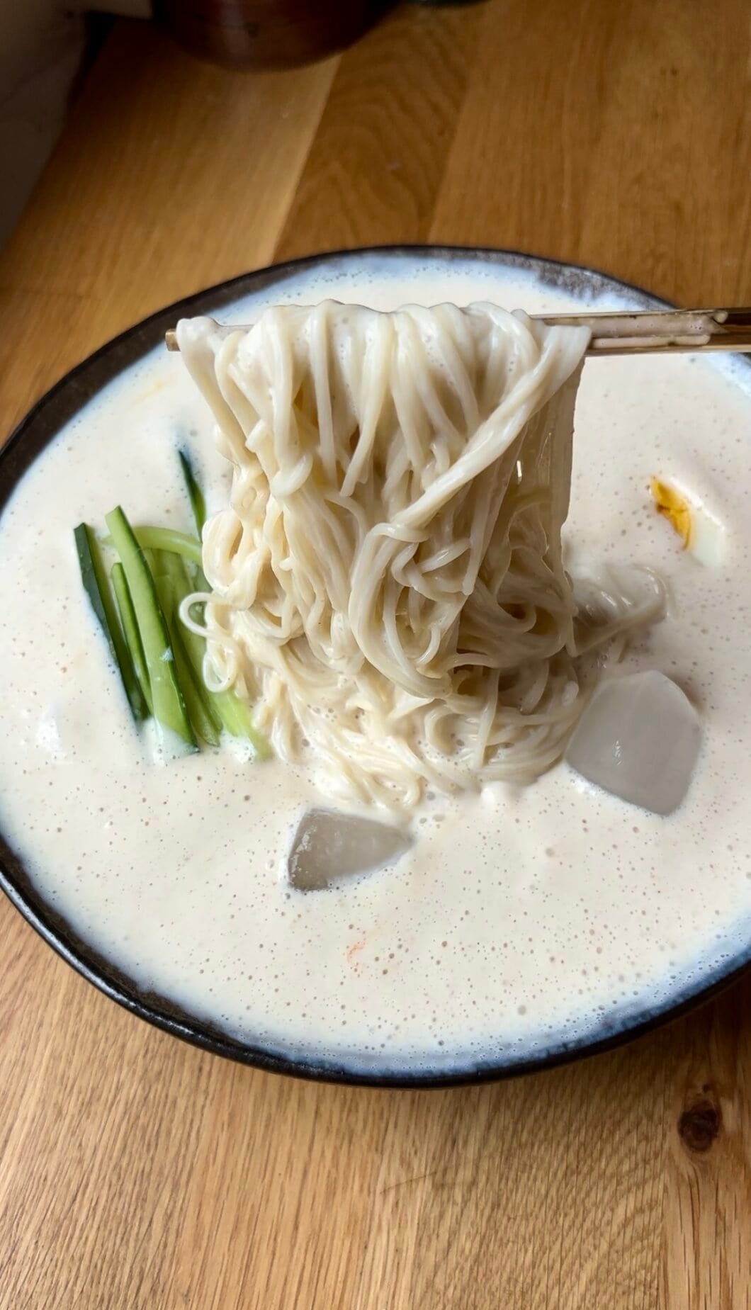 Milky white noodle soup with thin somen noodles, thin cucumber sticks and a halved boiled egg