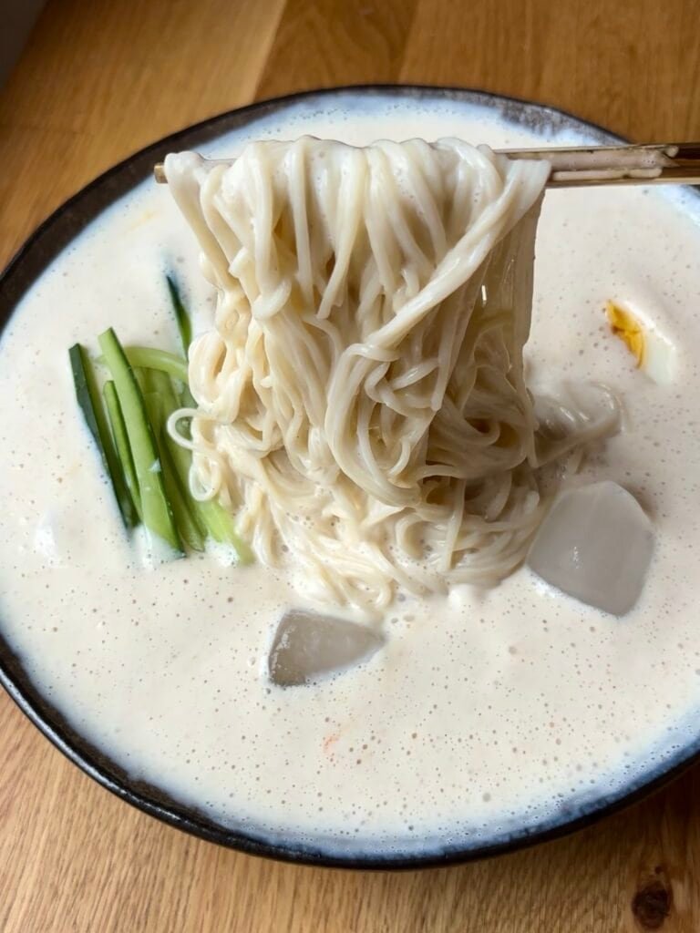 Milky white noodle soup with thin somen noodles, thin cucumber sticks and a halved boiled egg