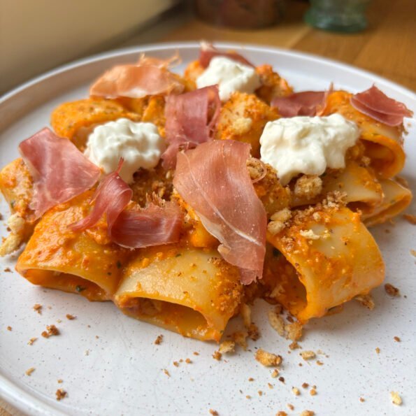 Mezzi paccheri pasta in pesto rosso topped with straciatella, pangrattato and parma ham