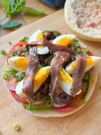 Pan Bagnat opened with tomato slices, green onion, radishes, eggs, tuna and anchovies, and lots of olive oil